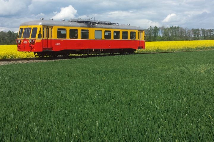 a passenger bus that is sitting on a train track near a grassy field