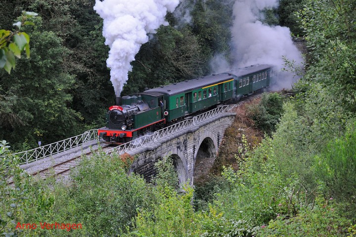 a steam engine train traveling down train tracks near a forest