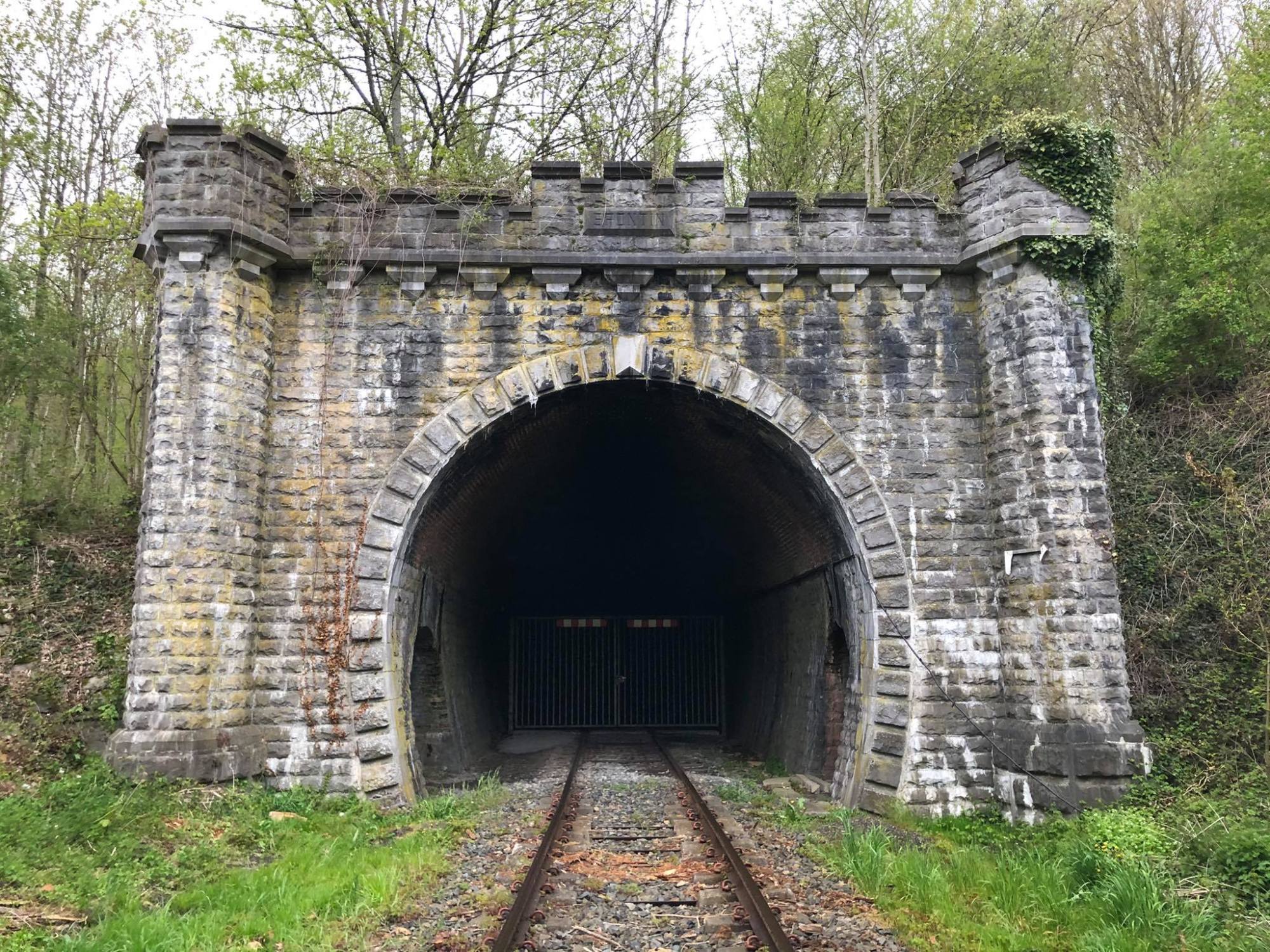 a stone building that has grass in front of a brick wall with Staple Bend Tunnel in the background