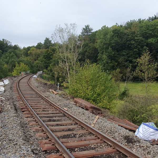 Railroad track curving into forested area with signal pole and construction materials nearby.