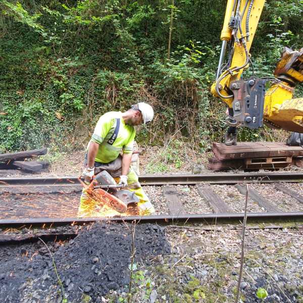 Worker in safety gear cutting railway track with sparks flying.