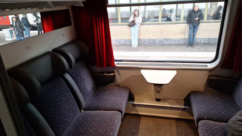 Train compartment with four seats and window showing people on platform.