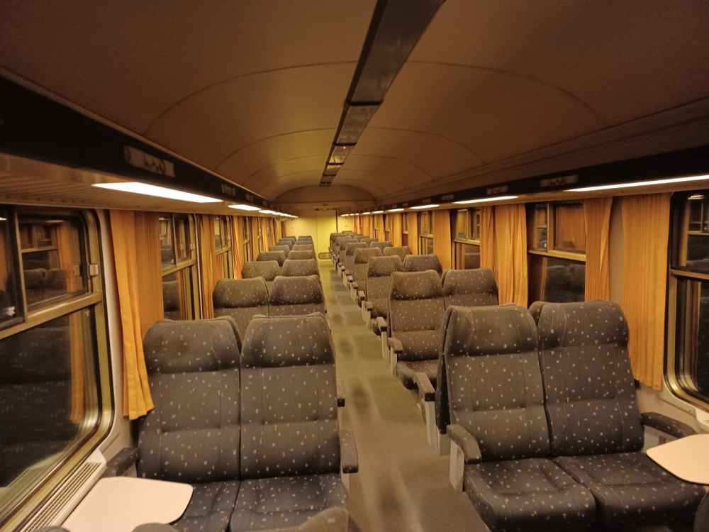 Empty train carriage with rows of blue seats and orange curtains, viewed from the aisle.