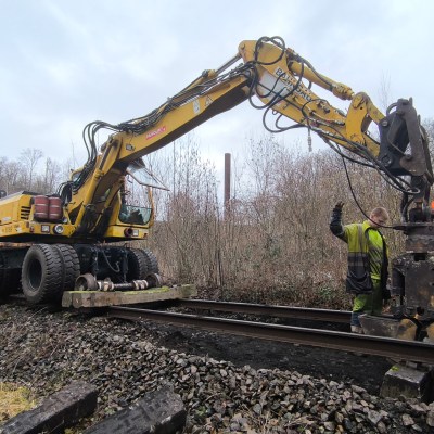 Workers using a heavy machine to install or repair railway tracks in a forest area.