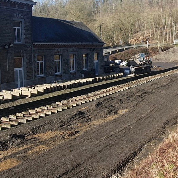 Railway construction site near a stone building and tunnel with tracks and gravel piles.