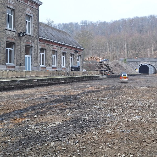 Old train station with a dirt path, forested hills, and a tunnel in the background.