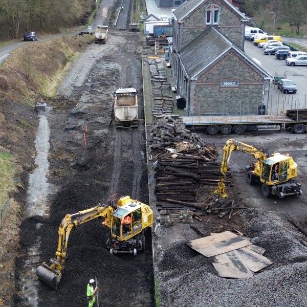 Construction site with excavators near a building and railway tracks.