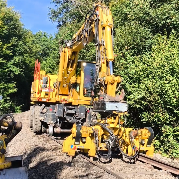 Yellow railway maintenance machine on tracks surrounded by greenery.