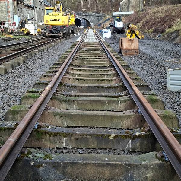 Railway track under construction with machinery and tunnel in the distance.