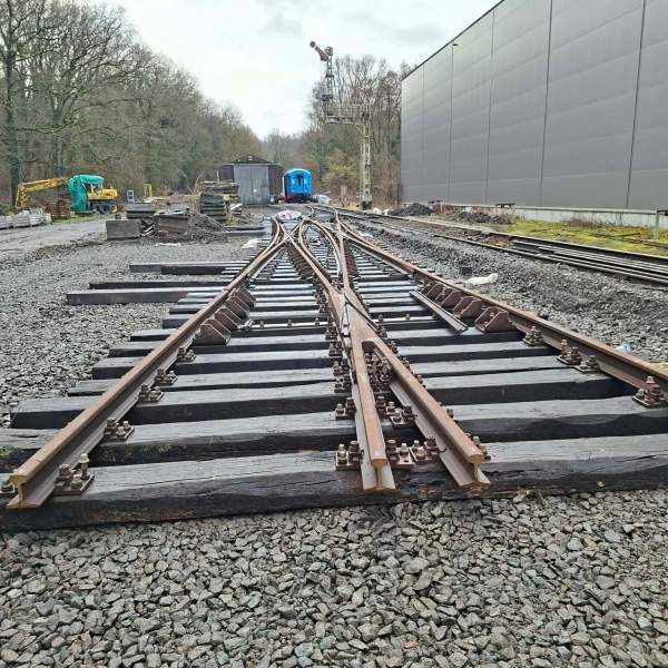 Railroad tracks diverging into two directions near industrial buildings and forested area.