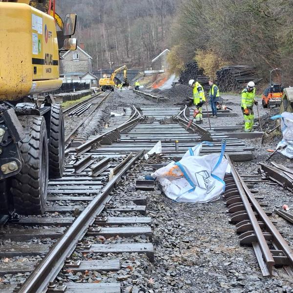 Construction workers repairing railway tracks with machinery and materials on-site.