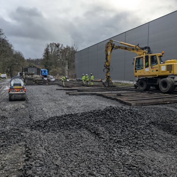Construction site with heavy machinery and workers laying railroad tracks on a cloudy day.