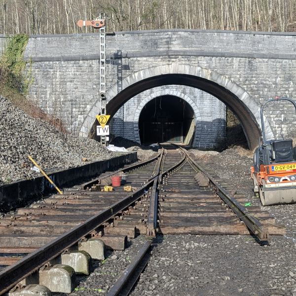 Railway tracks leading to a tunnel with a roller compactor nearby.