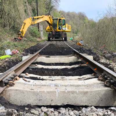 Construction machine working on railway tracks in a forested area.