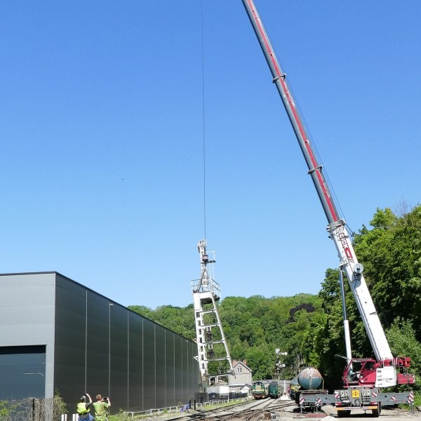 Large crane lifting structure by railway tracks, clear blue sky.