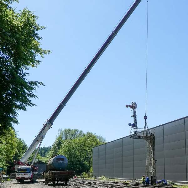 Large crane lifting a railroad signal tower next to train tracks with blue sky.