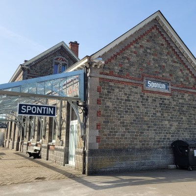 Historic brick train station with 'SPONTIN' signs and a glass canopy.
