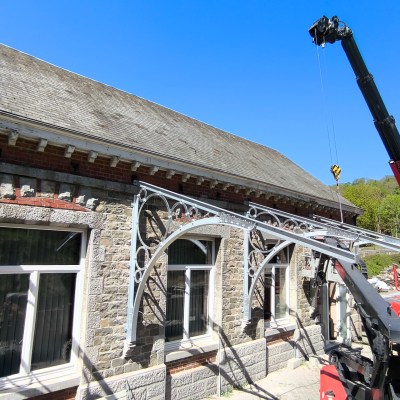 Construction site with crane lifting metal structure near stone building.