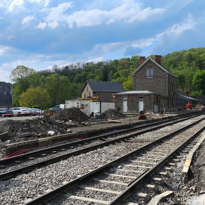 Railway tracks leading to a station with buildings and cars, surrounded by trees.