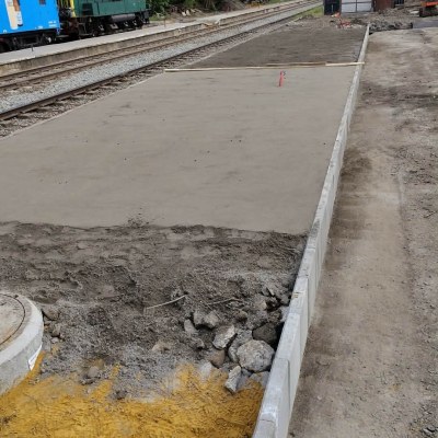 Construction site beside train tracks with fresh concrete and a blue train car.