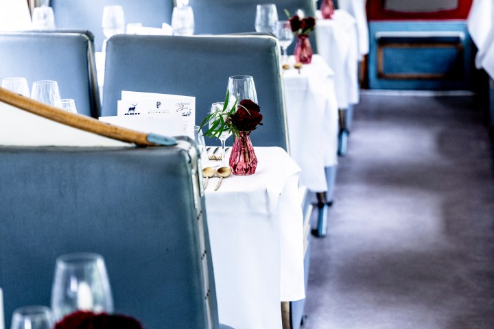 Elegant train dining car with tables set, white linens, and red flowers.