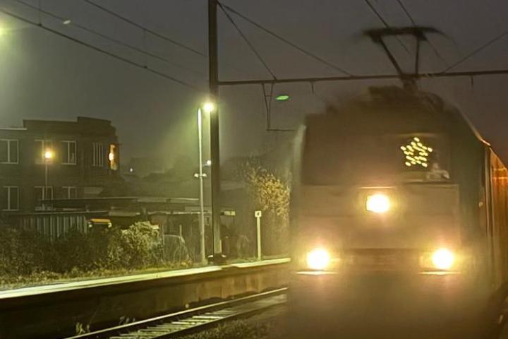 Train with headlights approaches a foggy station at night.
